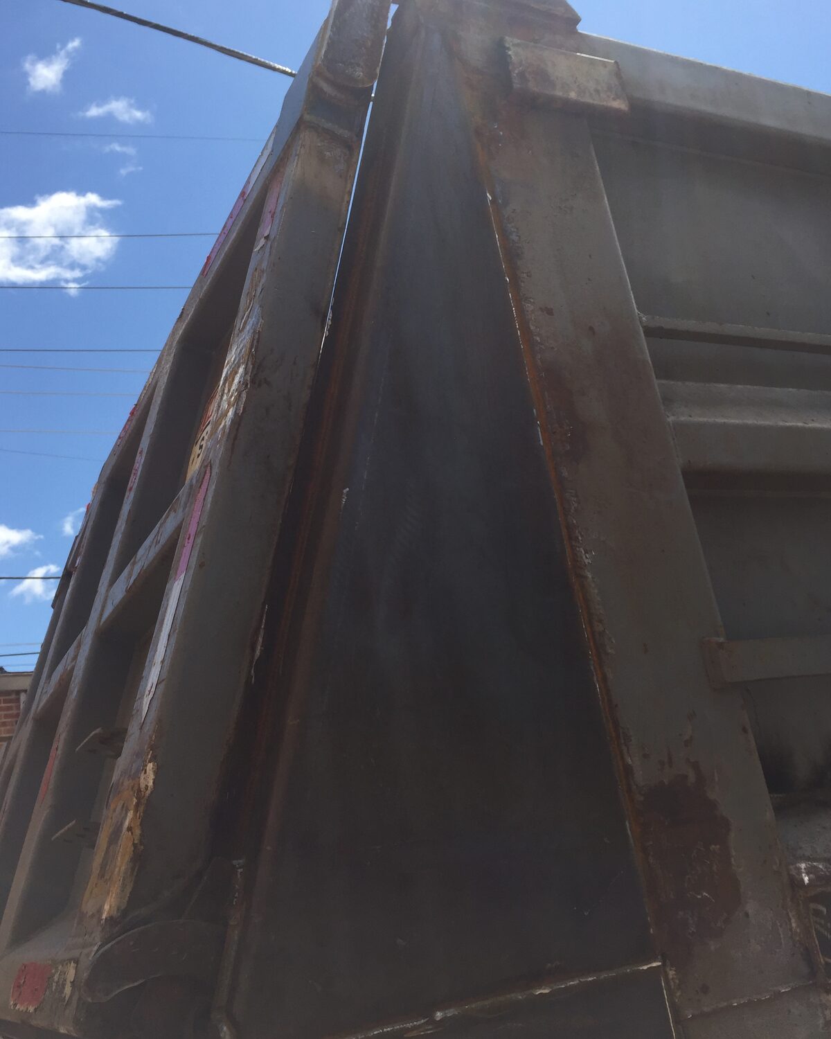 The same end-dump body's rear corner gusset brace after EMS refinishing — clean dark steel with fresh weld beads laid down the seams.
