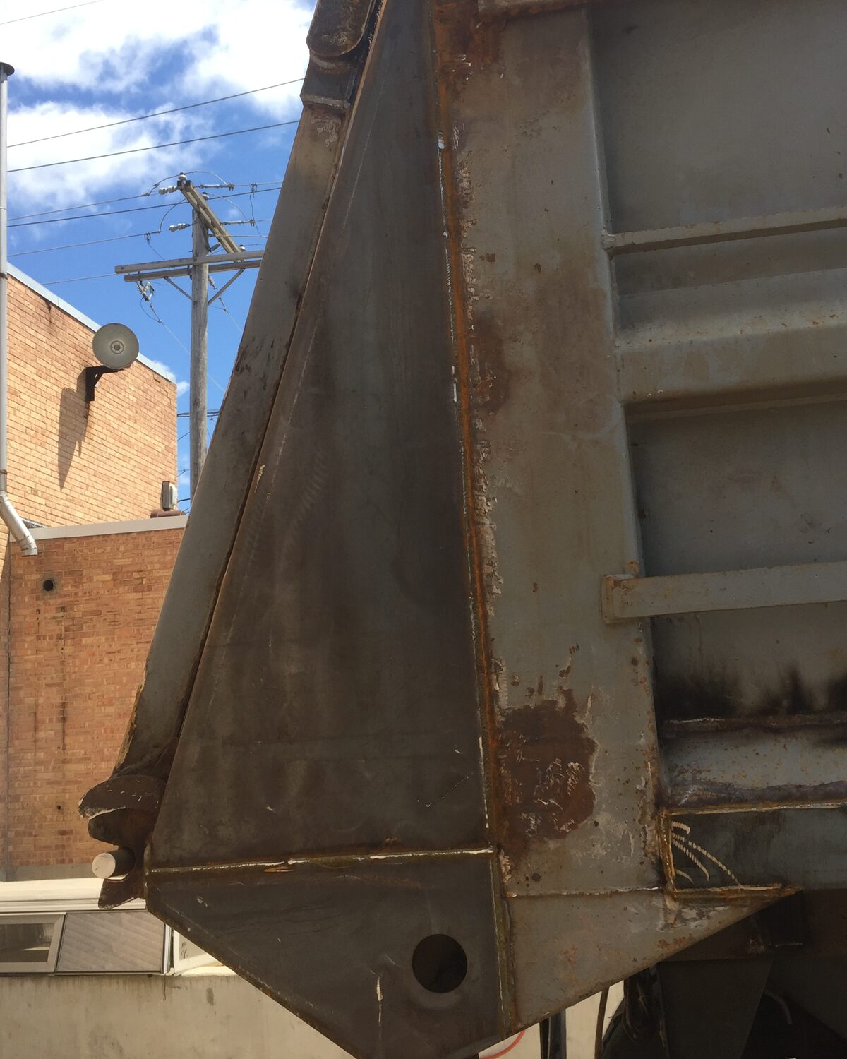 Weathered rear corner gusset brace on an end-dump body — flaking paint and rust streaking the welds, before refinishing.